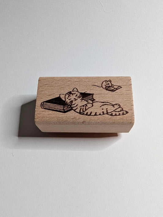Wooden stamp with a design of a cat reading a book on a white background